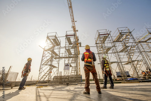 Construction engineers supervising progress of construction project stand on new concrete floor top roof and crane background