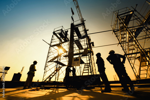 Construction engineers supervising progress of construction project stand on new concrete floor top roof and crane background