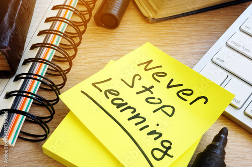 Never stop learning written on a memo stick. Lifelong learning concept.