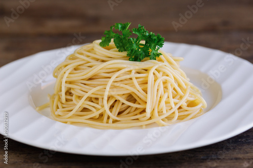 Boiled spaghetti with al dente level. Cooked pasta prepared for cooking on white plate decorated with fresh parsley in close up view on wood table. Homemade Italian traditional food concept.