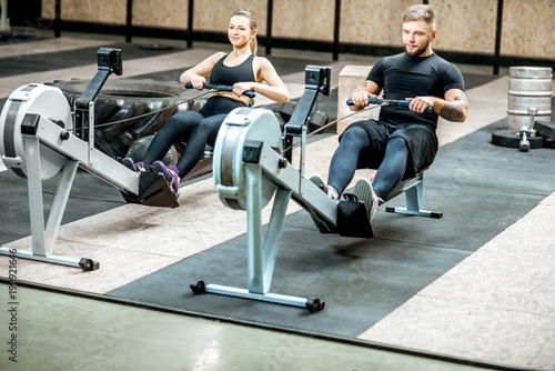 Young and beautiful couple training with exercise rowing machines in the gym