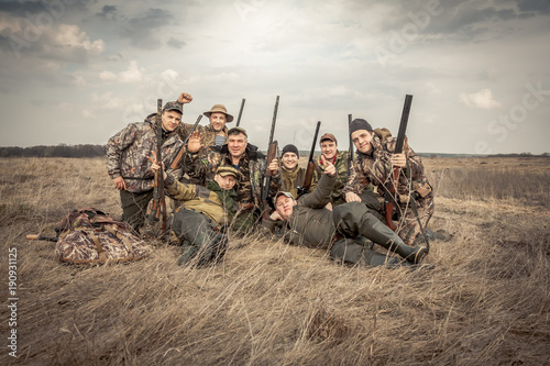 Men hunters group team portrait in rural field posing together against overcast sky during hunting season. Concept for teamwork