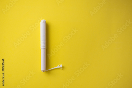 Feminine tampon with paper applicator on yellow background