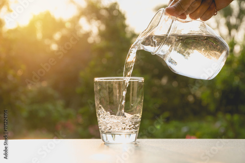 Person pouring water from pitcher to glass on nature background