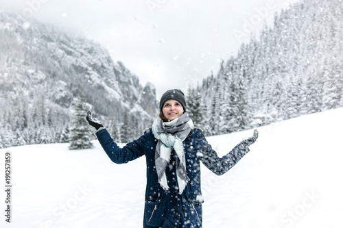 Uśmiechnięta dziewczyna rzuca śniegiem w górach zimą.