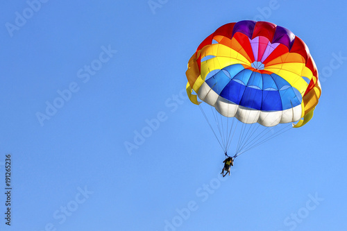 Two men are gliding using a parachute on the background of the blue sky.