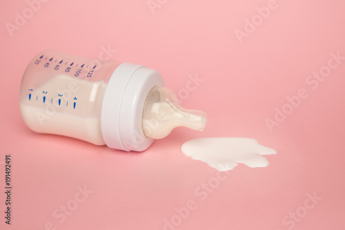Baby milk bottle on a pink background with neagtive space. Spill