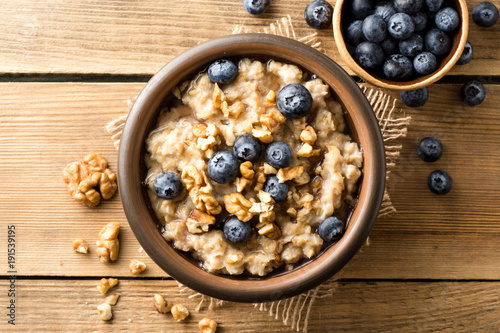 Oatmeal porridge with blueberries, walnuts and honey in ceramic bowl on wooden background.