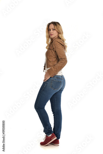 full length portrait of blonde girl wearing simple brown jacket and jeans, standing pose on white studio background.