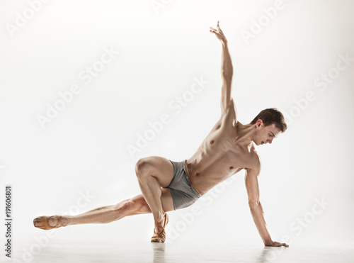 Athletic ballet dancer in a perfect shape performing over the grey background.