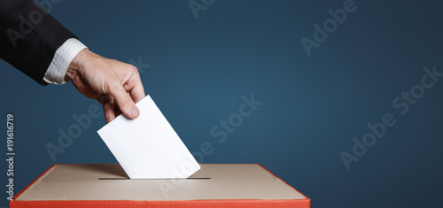 Voter Holds Envelope In Hand Above Vote Ballot On Blue Background. Freedom Democracy Concept