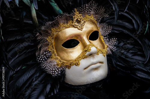 Detailed close-up photo of a gold and white venetian style renaissance mask with shiny black featheres