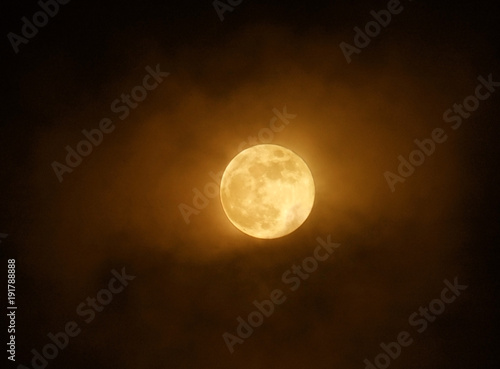 red full super moon glowing against clouds in a dark sky