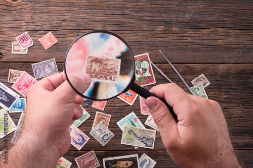 Stamp-collector. The philatelist looks at the old postage stamps. Collectible postage stamps on a wooden table.