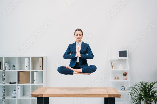 young businesswoman with closed eyes meditating while levitating at workplace