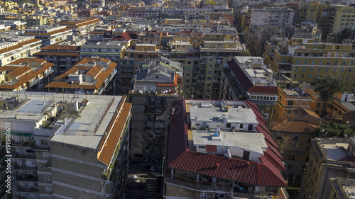 Aerial view of a group of buildings in the Tuscolana district in Rome, Italy. The roofs are passable and with antennas and TV. down the sunlit streets there are cars and trees.