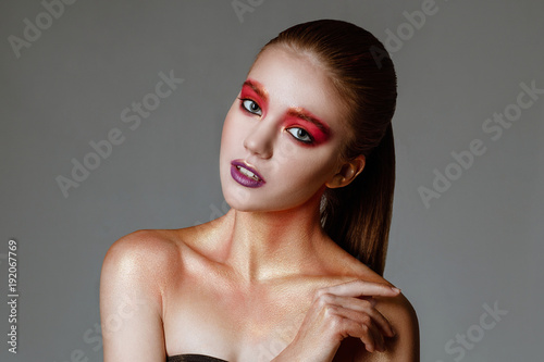 Girl's portrait close up. Beautiful woman with fashion bright makeup of eyes and creative violet lips. Photoshot in studio on a white background. with sparkles on her face.