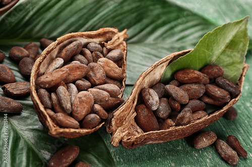 Halves of cocoa pod with beans and green leaves on wooden background