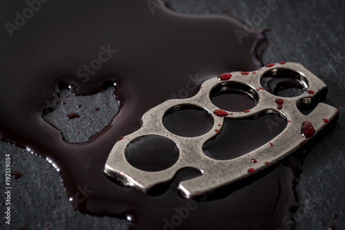 Gear and weapon used in illegal fighting, street violence and crime concept with metal knuckle sometimes called brass knuckles covered in blood with copy space