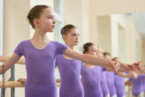 Close up young ballerinas practicing ballet. Group of beautiful ballet girls doing ballet exercises at ballet barre in studio.