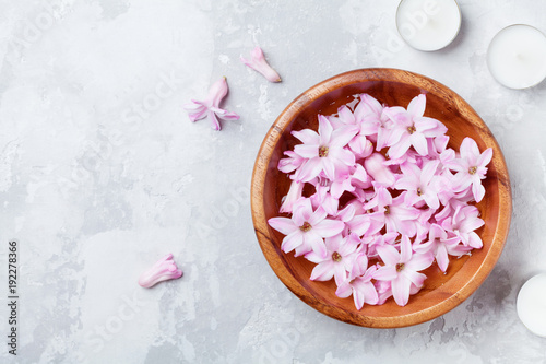 Beauty, spa and wellness composition of perfumed pink flowers water in wooden bowl and candles on stone table. Aromatherapy background. Top view, flat lay style.