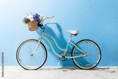 side view of bicycle with flowers in basket in front of blue wall