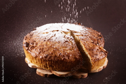 пирог стоит на чёрном фоне его посыпают сахарной пудрой 