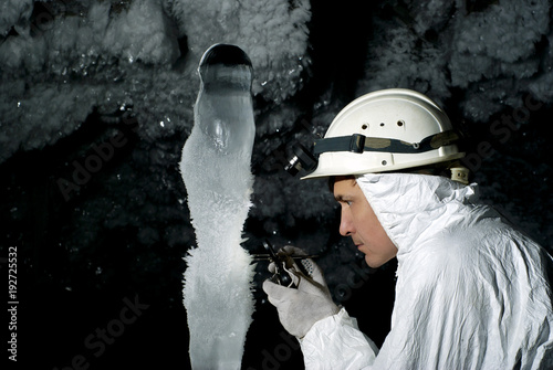 speleologist in a cave examines a giant ice stalagmite covered with hoarfrost, against a background of a dark rock covered with ice crystals