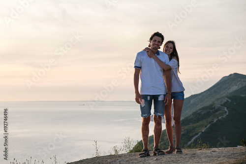 Woman hugging man on a mountain road with seascape at sunset. Front view.