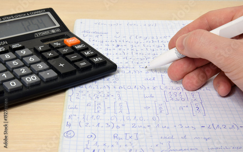 Solving math problems. Calculator, pen, hand.
