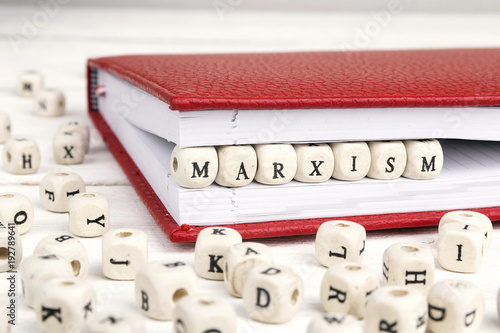 Word Marxism written in wooden blocks in red notebook on white wooden table.
