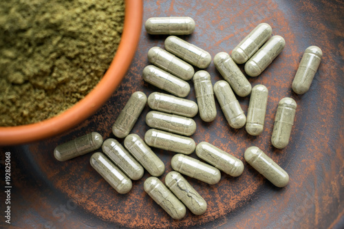 Close up Green capsules and powder on a clay brown plate on a burlap rustic background. Dietary supplements, vitamins and minerals for vegans and vegetarians. Healthy lifestyle, superfood