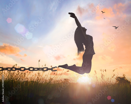 Freedom concept: Silhouette of a woman jumping and broken chains at orange meadow autumn sunset with her hands raised