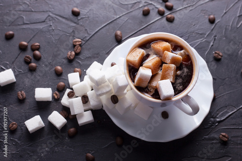 Sugar addict. Heap overabundance of sugar in a cup of coffee on a black table with scattered coffee beans