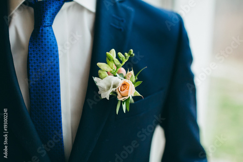 Close up image of beautiful boutonniere on the groom's jacket. Soft focus on boutonniere. Artwork