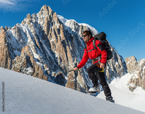 Young man in red jacket climbing up on glacier in big mountain