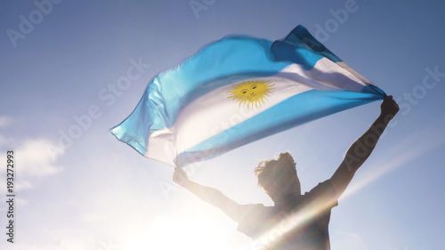 Young man holding argentinian national flag to the sky with two hands at the beach at sunset argentina