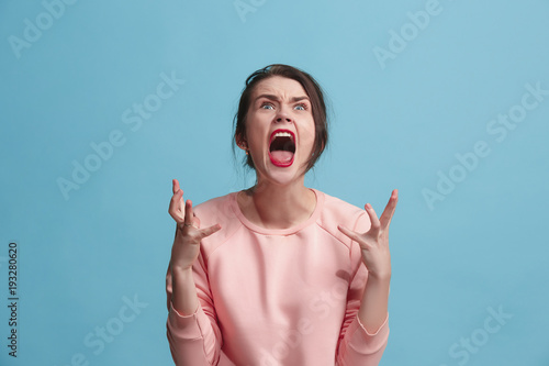 The young emotional angry woman screaming on blue studio background