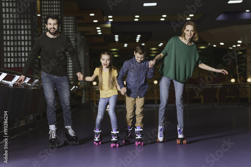 happy family holding hands while skating together on roller rink