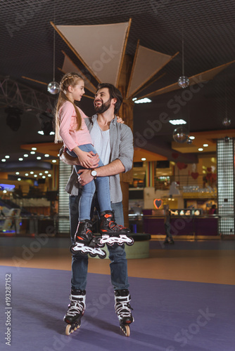 happy father holding daughter in roller skates on roller rink