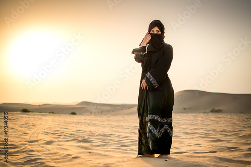 Full length portrait of Arab woman in burka clothing standing in the desert.