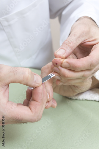 5. Kropelka krwi na palcu i dłonie lekarza z papierkiem do glukometru. Mierzenie cukru. 