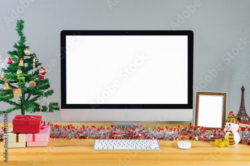 Merry Christmas and Happy New Year 2018! Celebrating holiday in modern office,Computer display on table with isolated white screen for mockup in x-mas time. Christmas tree with gifts decorations