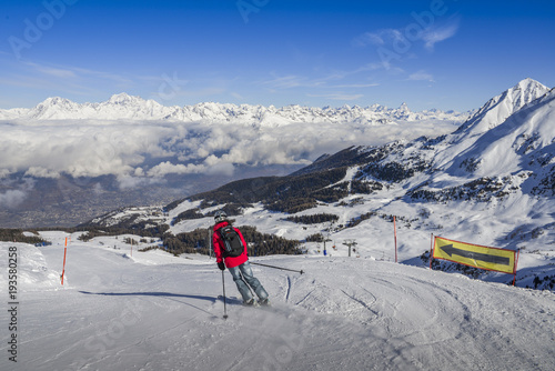One skier in jeans going downhill a piste with panoramic view of wide and groomed ski piste. View Towards north is Switzerland and its iconic Matterhorn