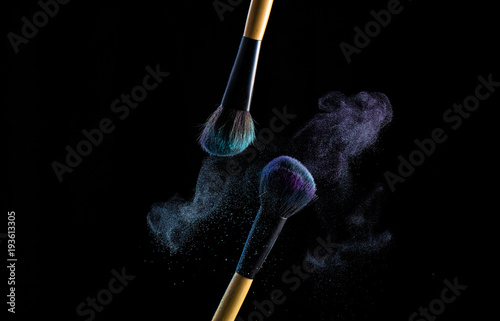 Two make up brushes with powder explosion dust in blue and purple color, close up