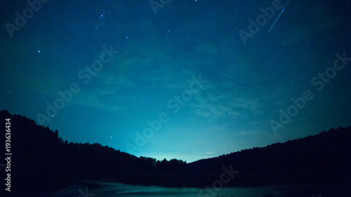 Stars over the lake at summer night on dark sky. Starfall. Amazing milky way galaxy with big amount of stars. Star trails, beautiful blue night, Star trails over the river and mountain