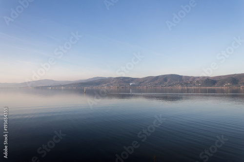 Beautiful view of Trasimeno lake (Umbria, Italy), with hills and blue sky reflecting on water