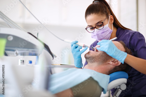Dentist drilling tooth to male patient in dental chair