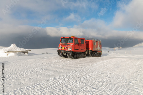 Red ratrak snowcat in winter mountains. A red snow tucker covered with snow.