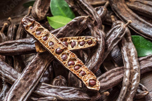 Carob pods and carob beans on the wooden table.